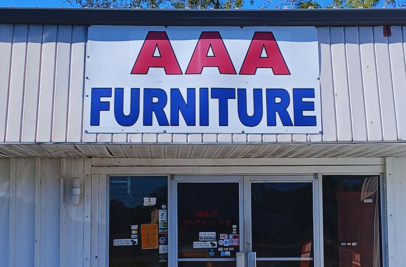 Sign for "AAA FURNITURE" on a storefront with a blue sky background.